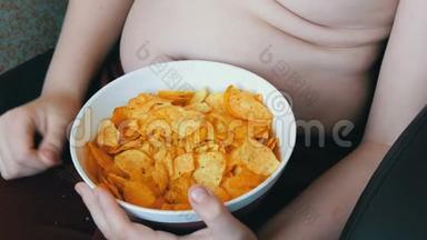 肥胖的少年身体上有脂肪褶皱，正在吃薯片.. 不健康食品，快餐.. 儿童`营养问题